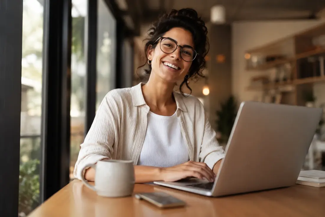 Woman smiling while working on a laptop in a cafe