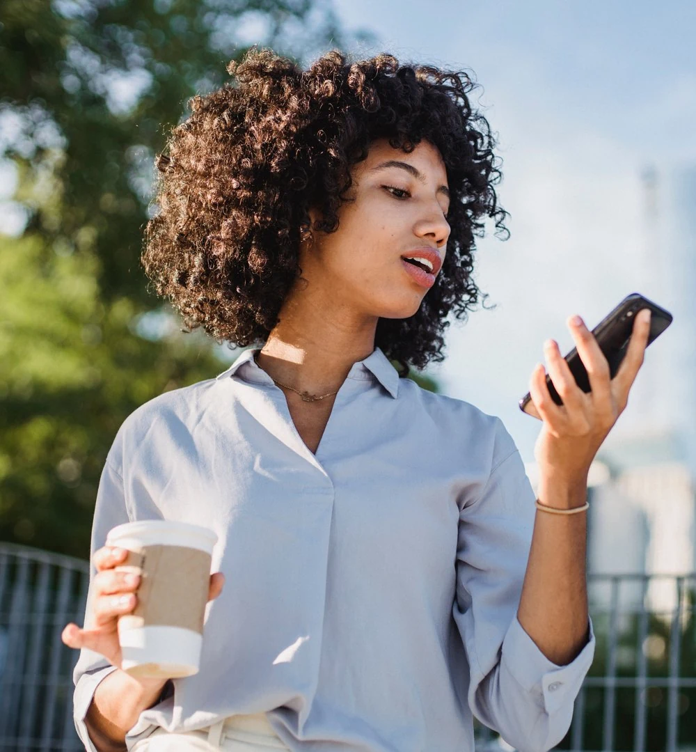 A woman in the city holding a coffee and looking at her phone