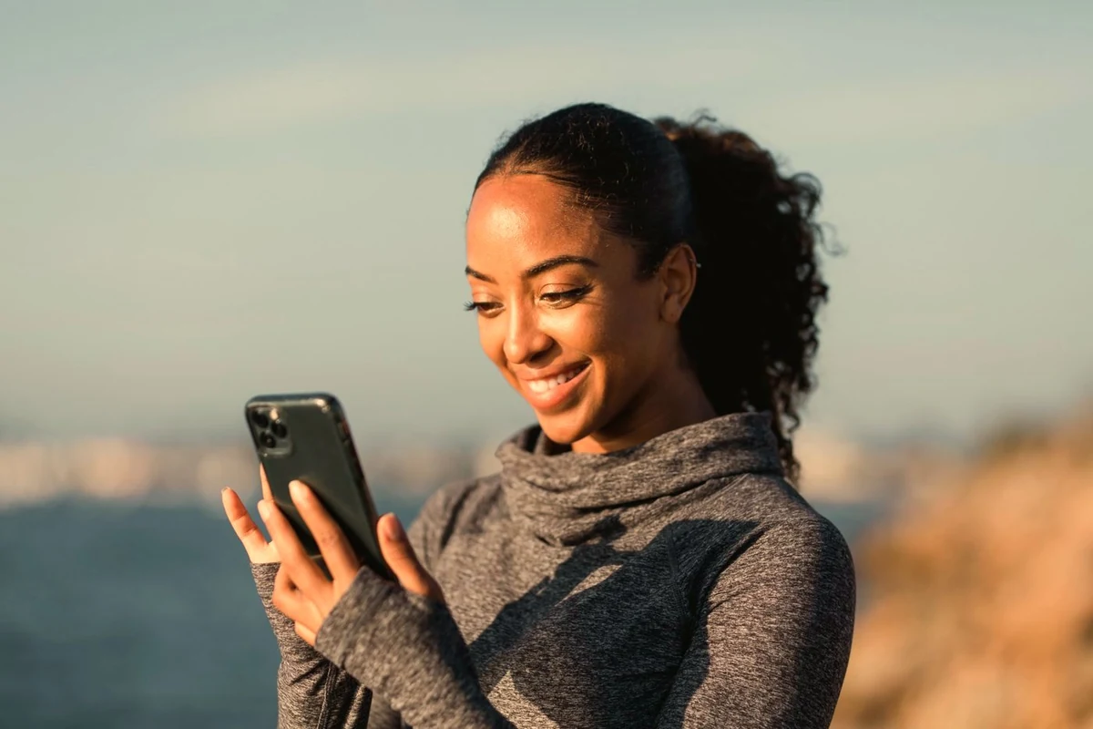 A woman by the water smiling at her phone