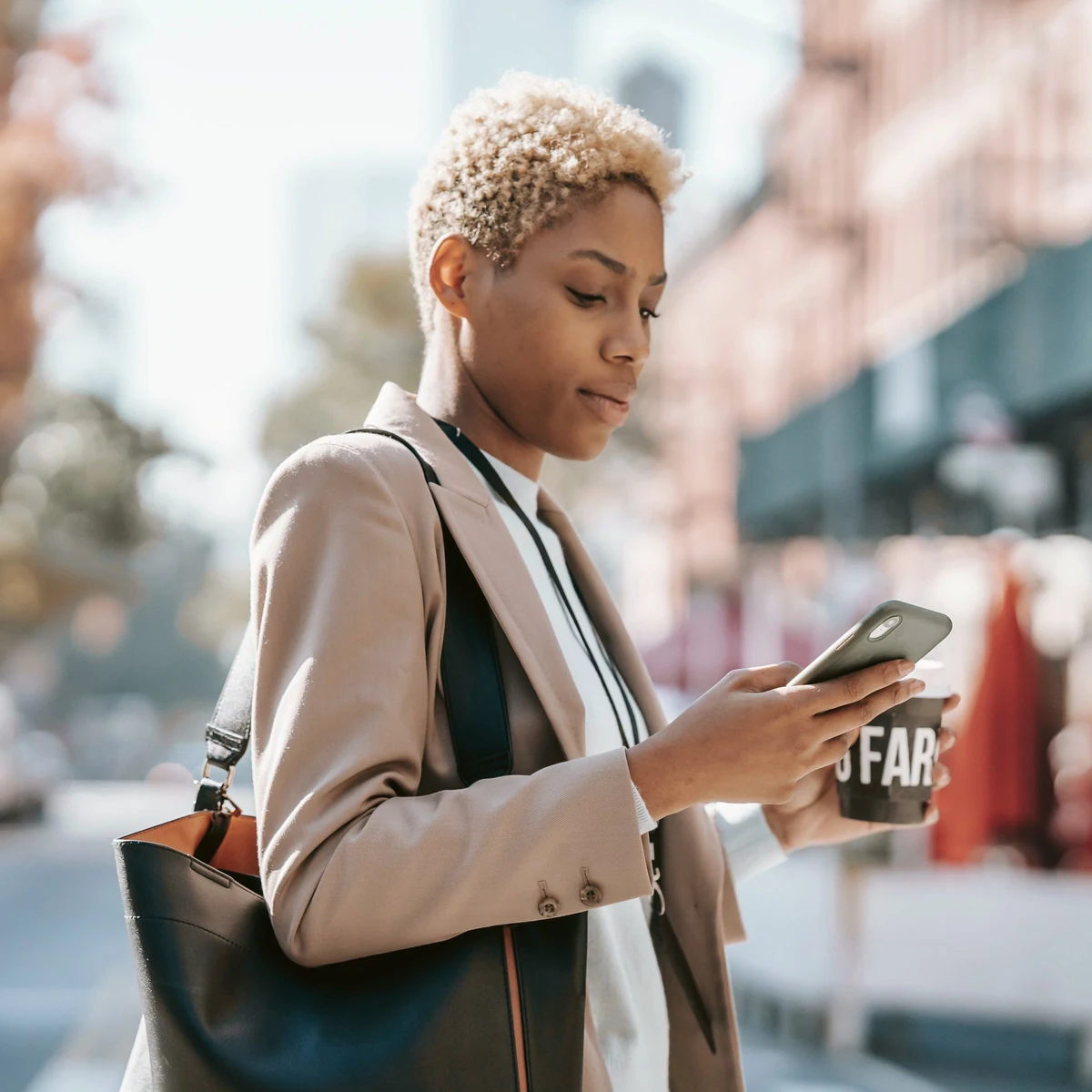 A woman with a coffee checking her phone on a sunny street